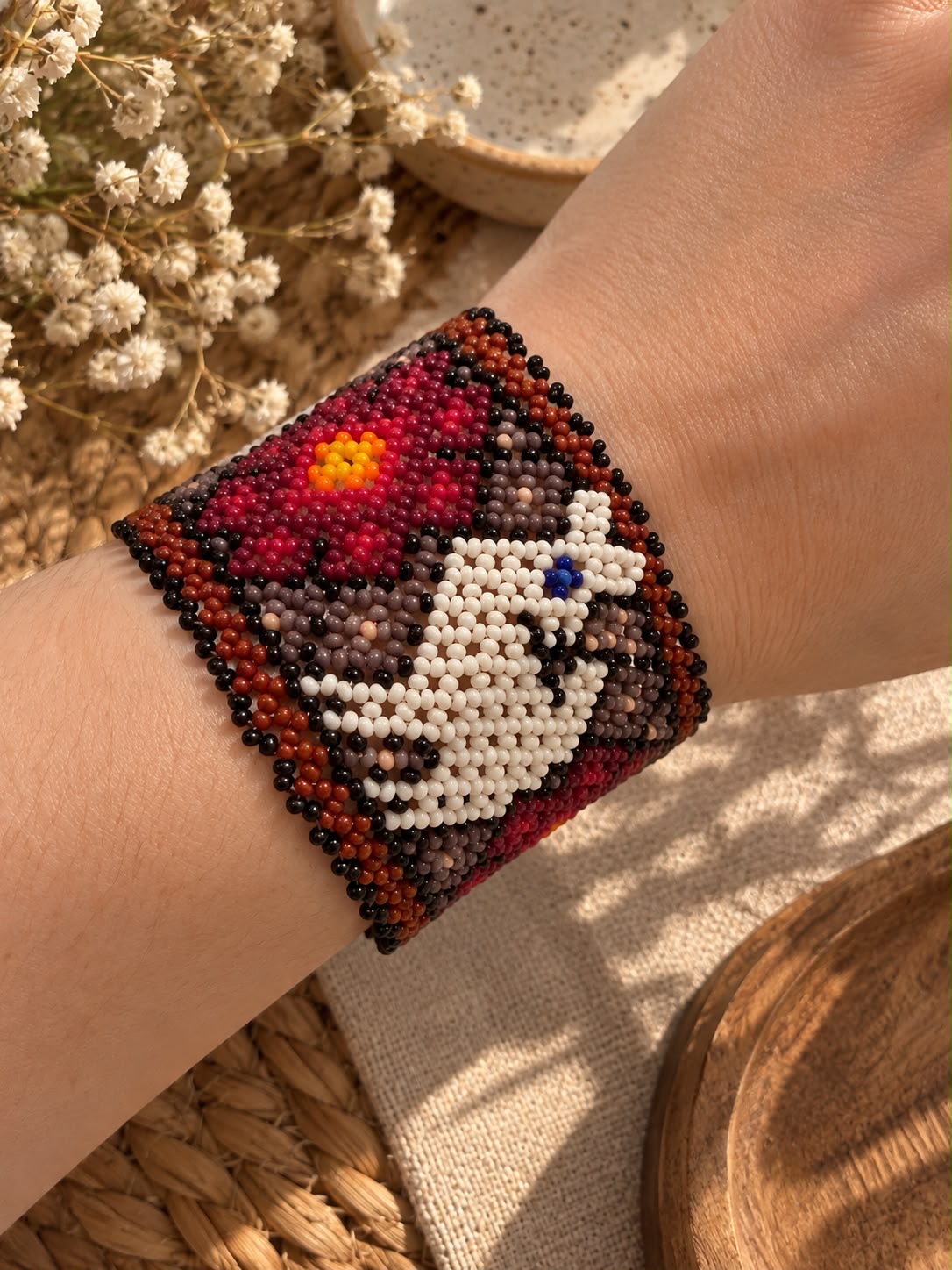 Beaded cuff with deep red flower and crisp white motif on a richly patterned dark neutral background